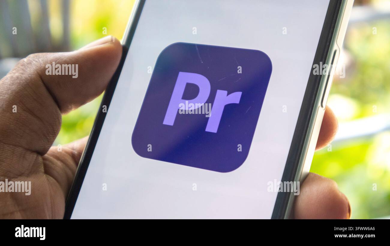 Persona che tiene un telefono cellulare che mostra l'icona di Adobe Premiere Pro. Interfaccia dell'applicazione di editing video. Strumento di produzione multimediale digitale sullo schermo. Nat sfocato Foto Stock