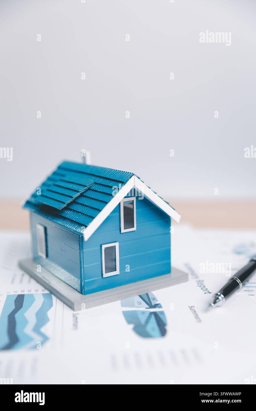 Una casa modello blu si trova su grafici stampati con una penna nera nelle vicinanze, lasciando un ampio spazio bianco sopra, illustrando una pianificazione abitativa o immobiliare c Foto Stock