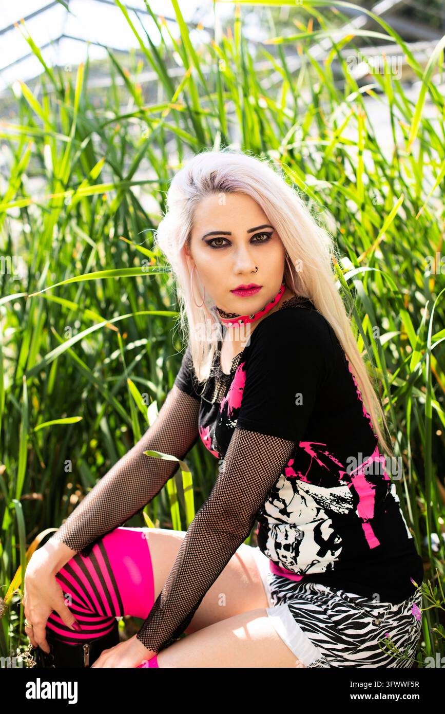 Bella donna ritratto con punk make up e vestito con i capelli decolorati in posa di un abbandonato casa verde dove la natura ha preso il suo pedaggio Foto Stock