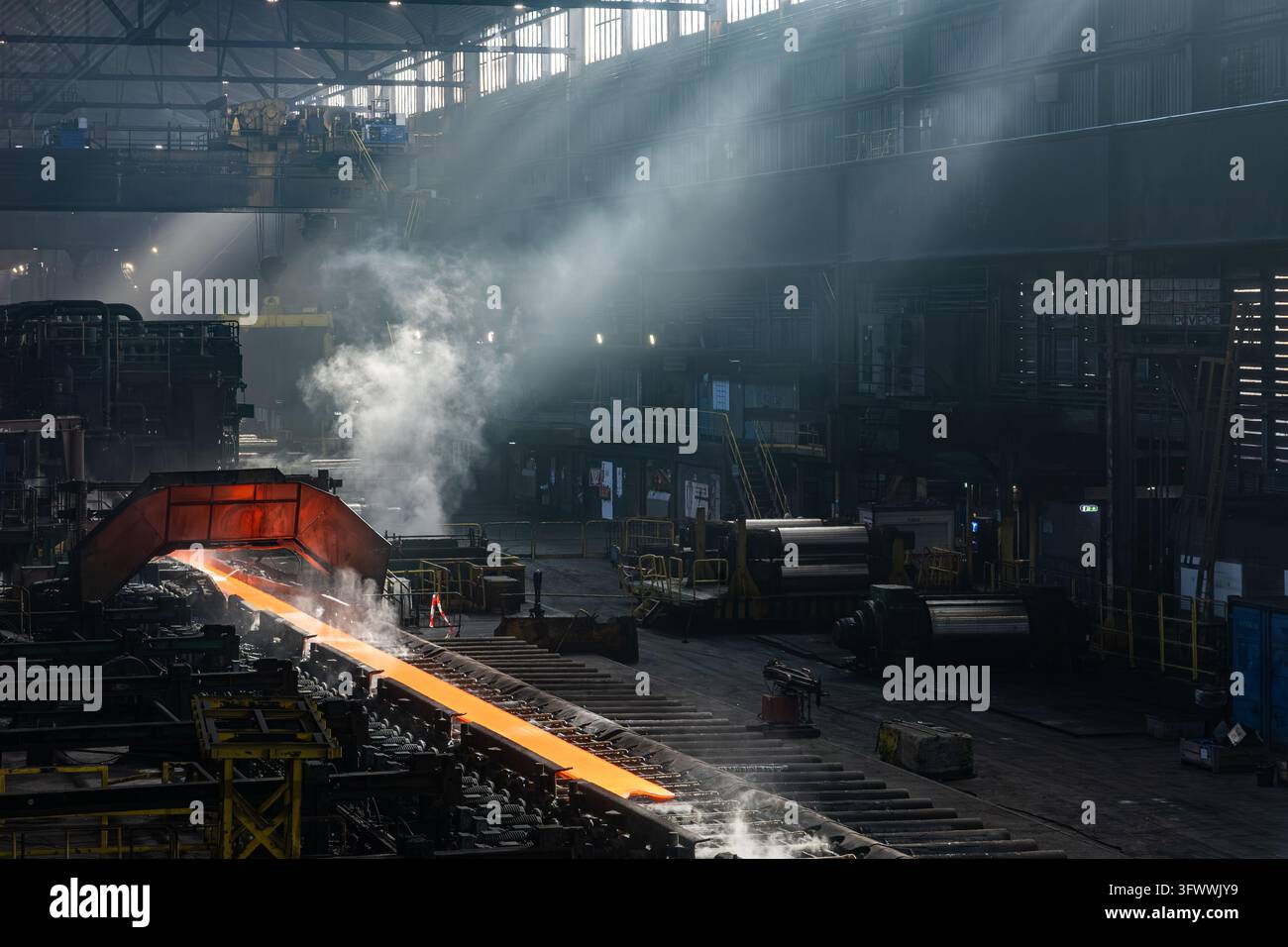 Vista dello stabilimento Tata Steel che mostra una piastra d'acciaio incandescente che si muove attraverso il laminatoio con vapore che sale nel capannone industriale, Velsen-Noord Foto Stock