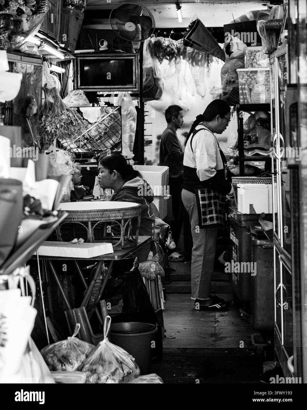 Chiang Mai, Thailandia - 17 gennaio 2026: Un'immagine in bianco e nero cattura l'interno di una bancarella di mercato affollata con tre individui tra oggetti appesi… Foto Stock