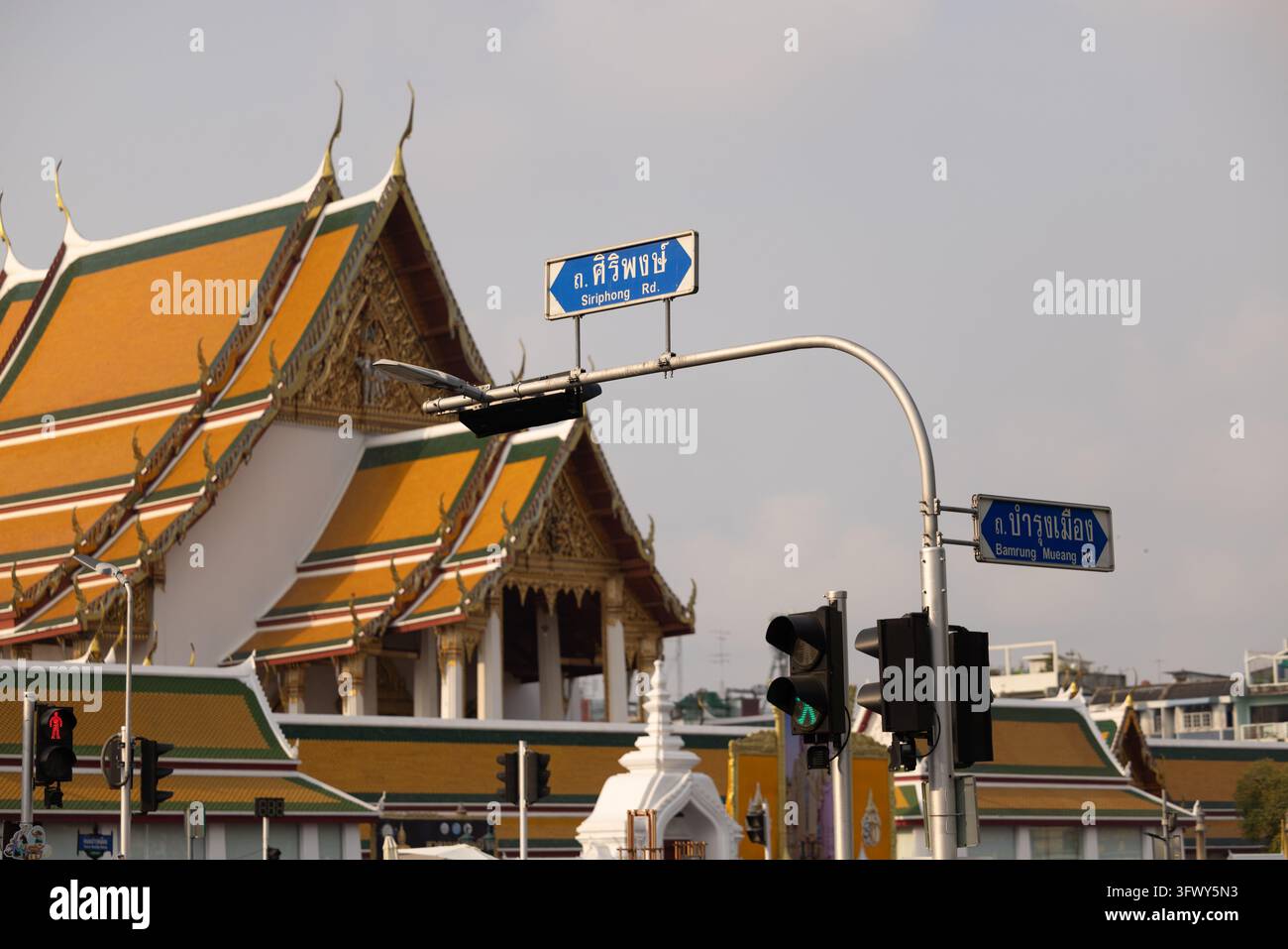 Bangkok, Thailandia - 31 gennaio 2026: Semofori e cartelli stradali a un incrocio con tetti di templi tradizionali ornati sullo sfondo... Foto Stock
