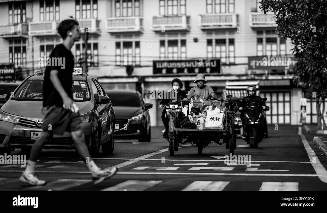 Bangkok, Thailandia - 31 gennaio 2026: Una foto in bianco e nero mostra un pedone che attraversa la strada, auto e motociclisti tra cui un... Foto Stock