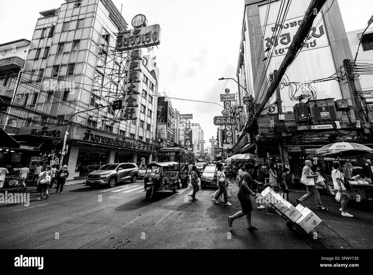 Bangkok, Thailandia - 31 gennaio 2026: Una vivace strada cittadina piena di pedoni che attraversano, veicoli tra cui un tuk-tuk e auto, circondata da... Foto Stock