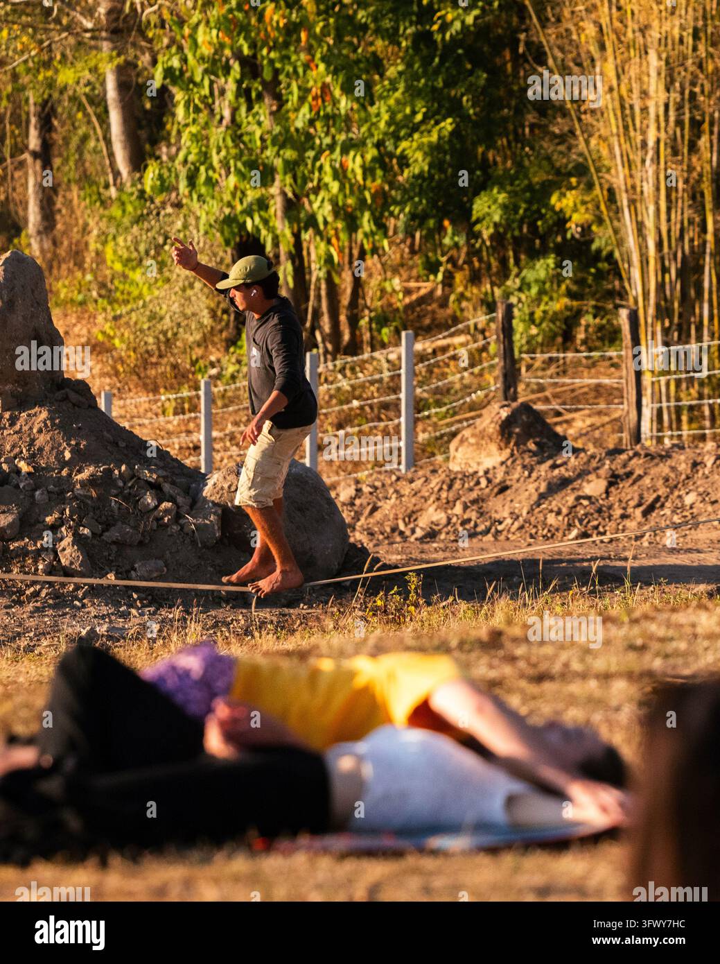 Pai, Thailandia - 22 gennaio 2026: Un uomo si bilancia a piedi nudi su una slackline all'aperto mentre altri riposano nelle vicinanze. Foto Stock