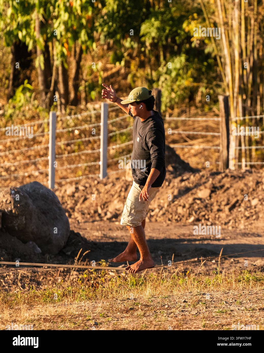 Pai, Thailandia - 22 gennaio 2026: Un uomo si bilancia a piedi nudi su una slackline all'aperto vicino a una recinzione e ad alberi. Foto Stock