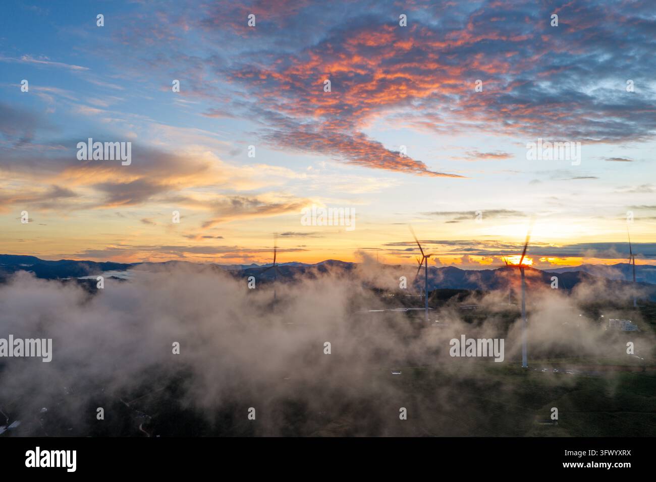 Vista aerea di turbine eoliche che si ergono sopra un mare di nuvole nel paesaggio montano di Da Lat, Lam Dong, Vietnam. Foto Stock