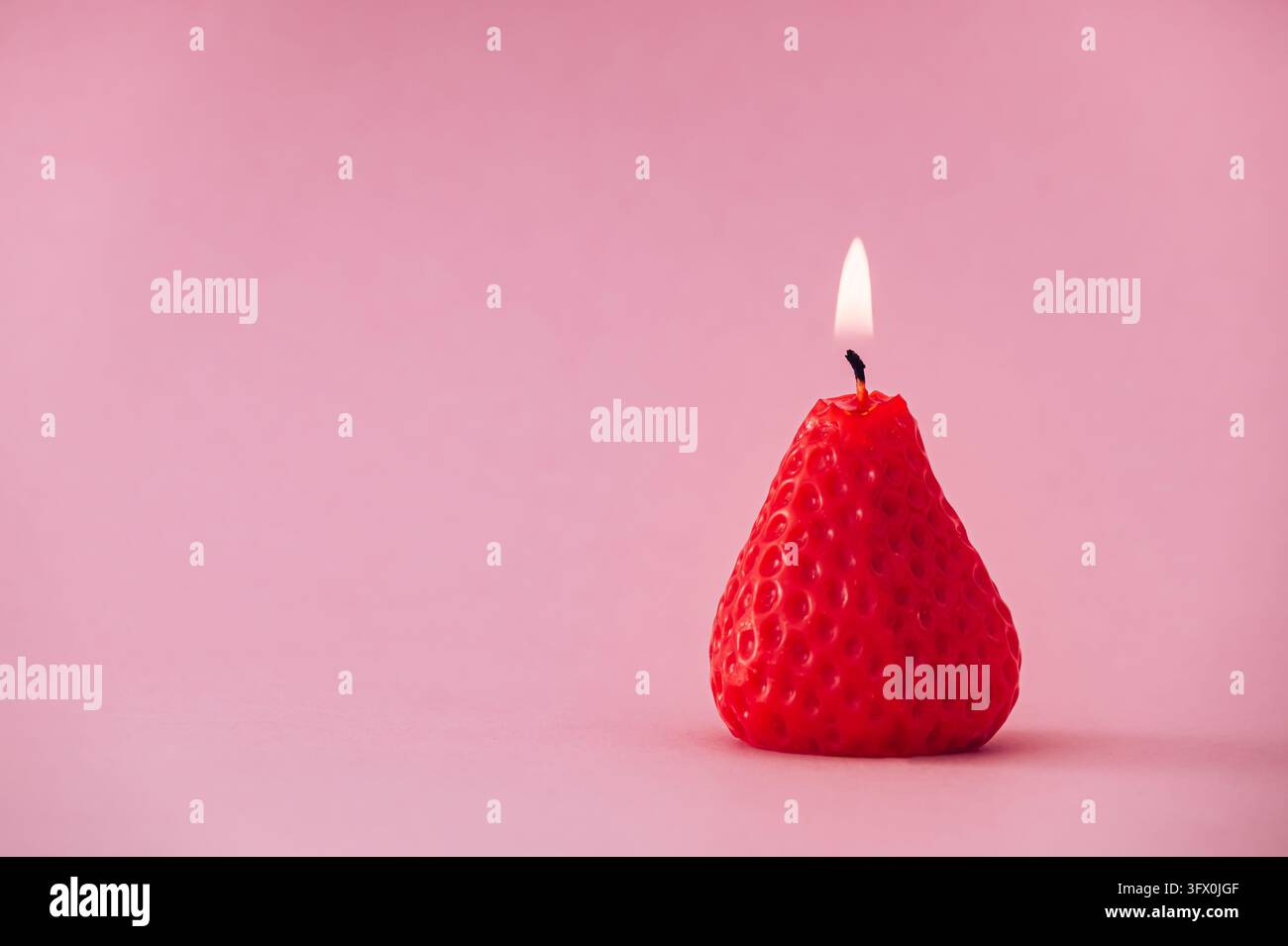 Candela a forma di fragola che brucia su sfondo rosa con spazio per il testo. Estetica estiva creativa e concetto di natura morta minimalista. Foto Stock
