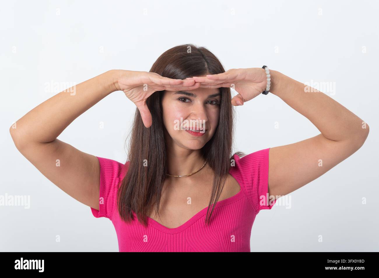 Giovane donna che crea una cornice attorno al suo viso con le mani, guardando direttamente la fotocamera con un sorriso sottile, ideale per concetti di selezione o pe Foto Stock