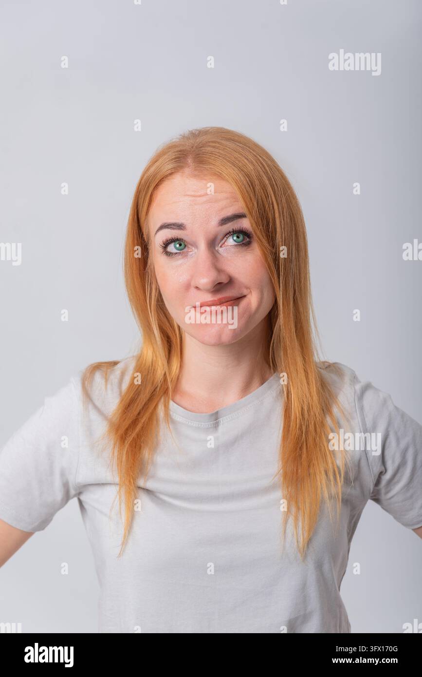 Giovane donna che alza le spalle con uno sguardo interrogativo, mostrando incertezza e un bisogno di chiarimento o risposta mentre guarda in alto con un'espressione leggermente perplessa Foto Stock