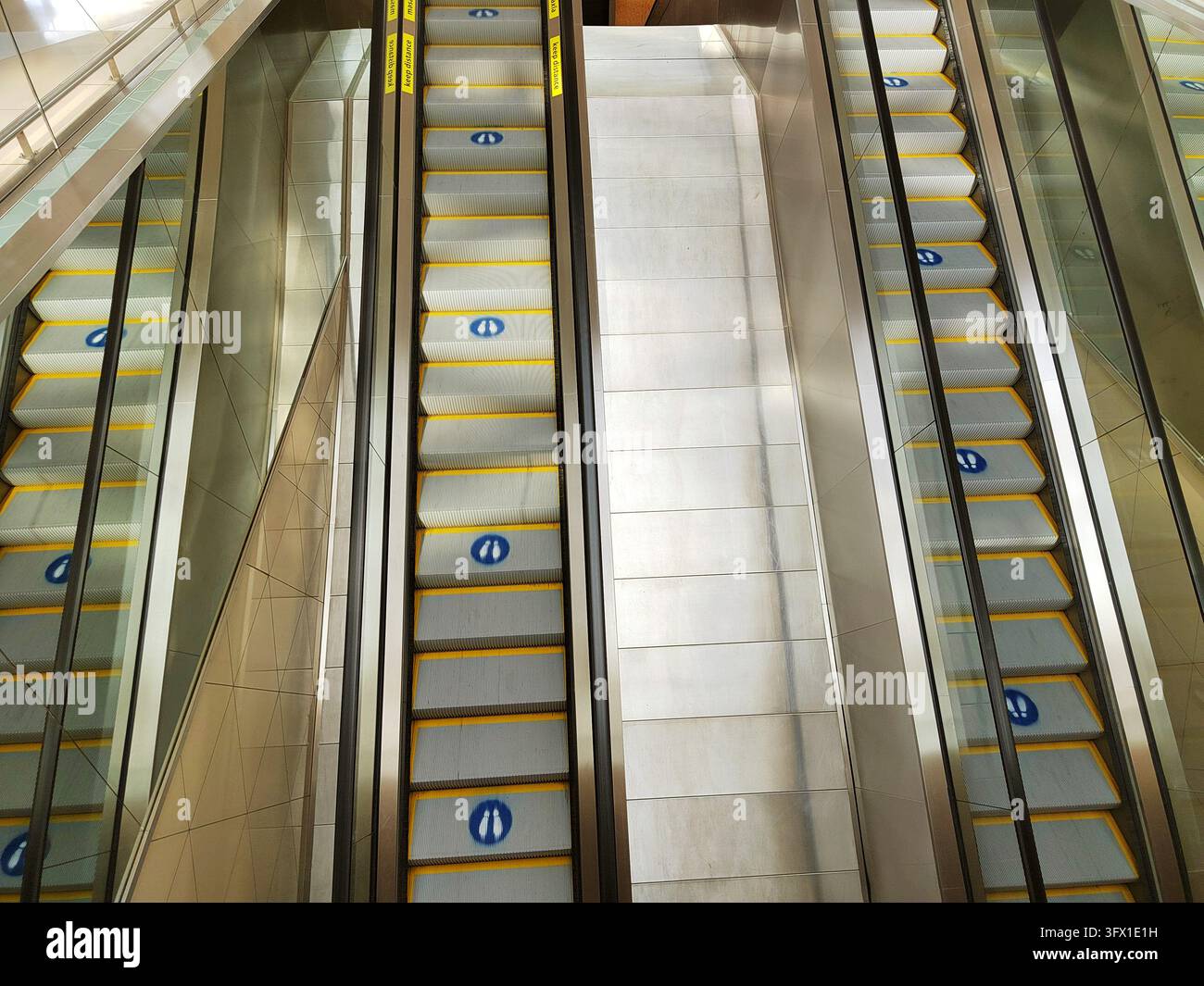Scale mobili parallele con gradini bordati di giallo scendono attraverso un interno luminoso, illustrando il traffico pedonale in un grande edificio pubblico Foto Stock