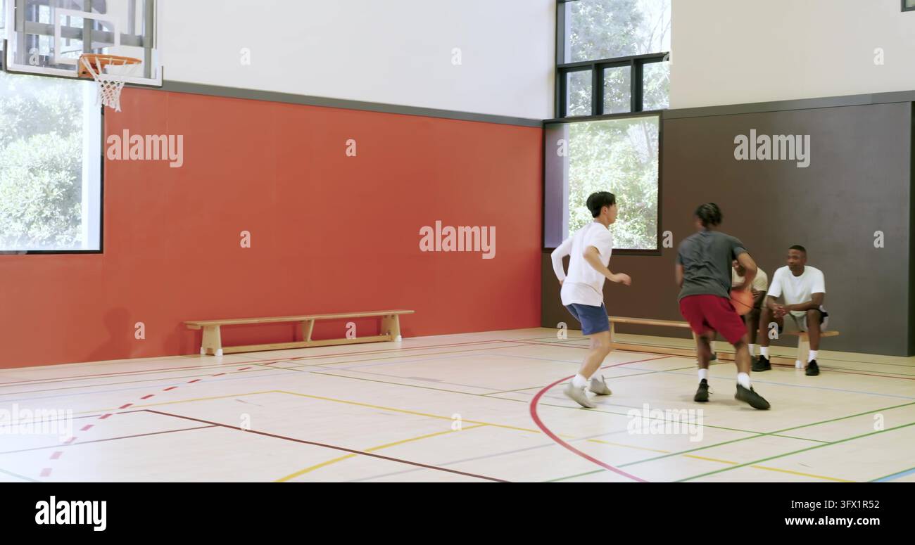 Diversi amici maschi che fingono di guidare, praticano crossover di basket, tirano canestri sul campo Foto Stock