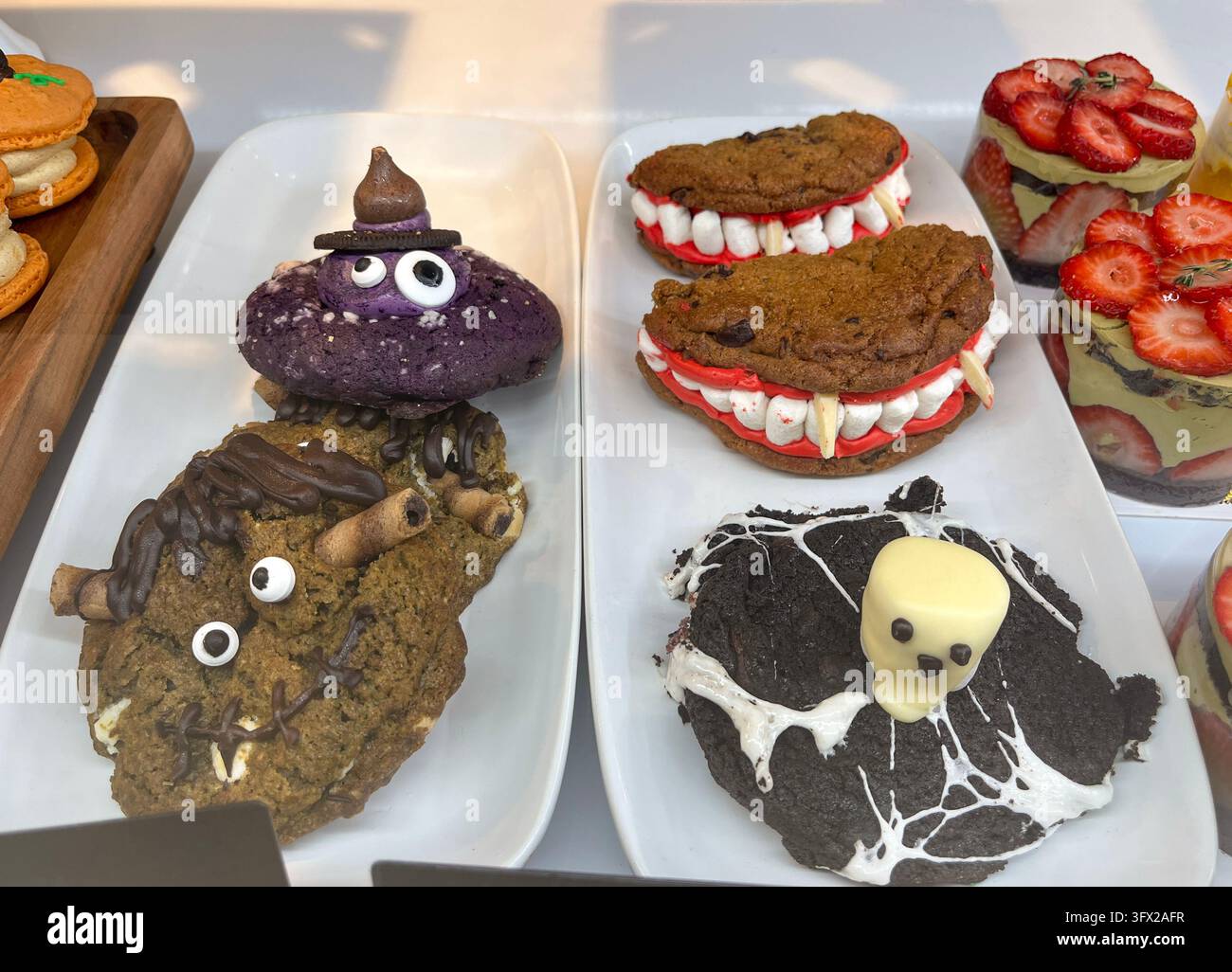 Esposizione in panetteria con piatti bianchi contenenti grandi biscotti decorati per Halloween a forma di strega, denti di vampiro e fantasma Foto Stock