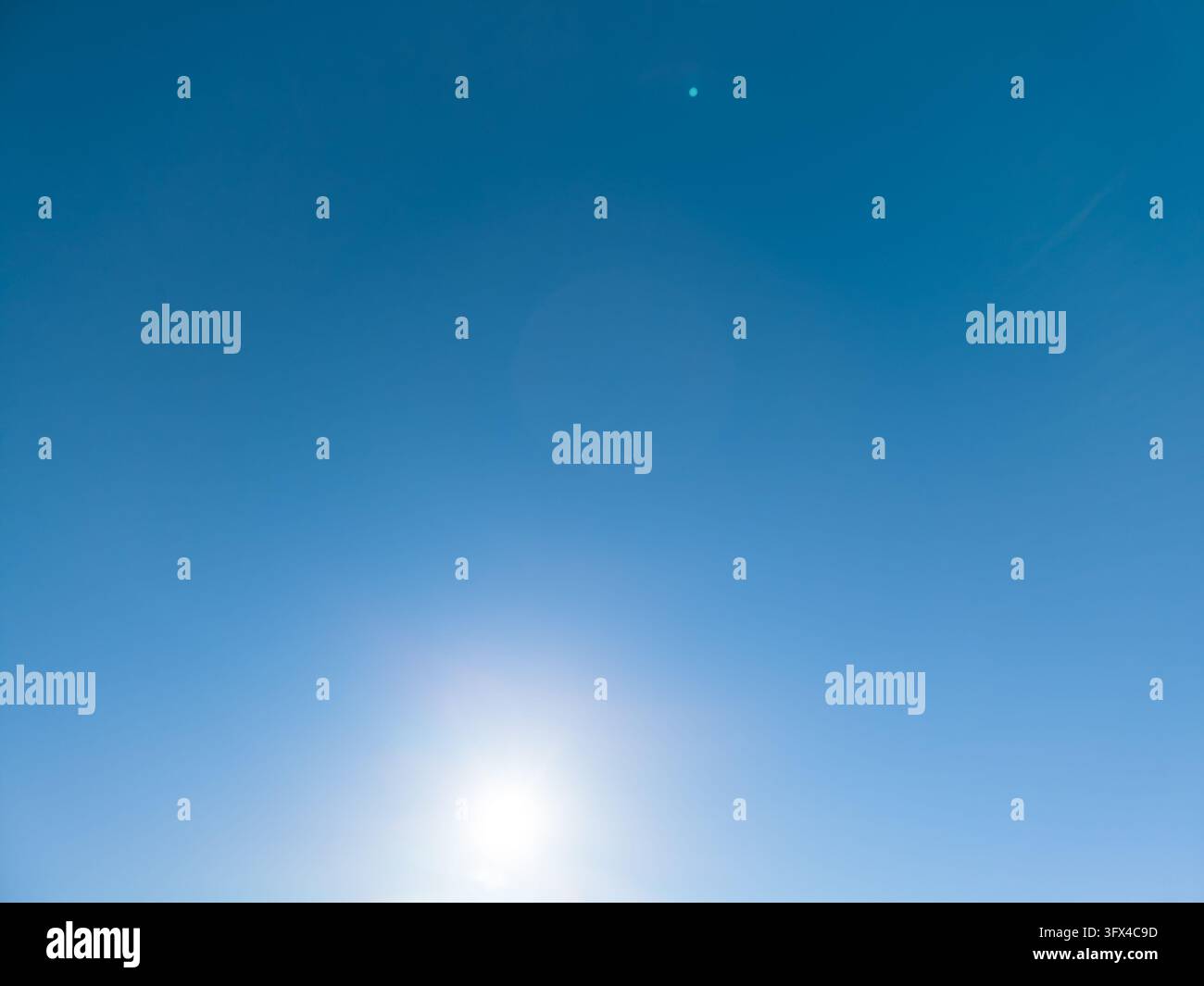 Sfondo di cielo blu brillante con il sole che splende vicino al bordo inferiore del fotogramma, una transizione di cielo liscia e chiara con bagliore della lente e Foto Stock