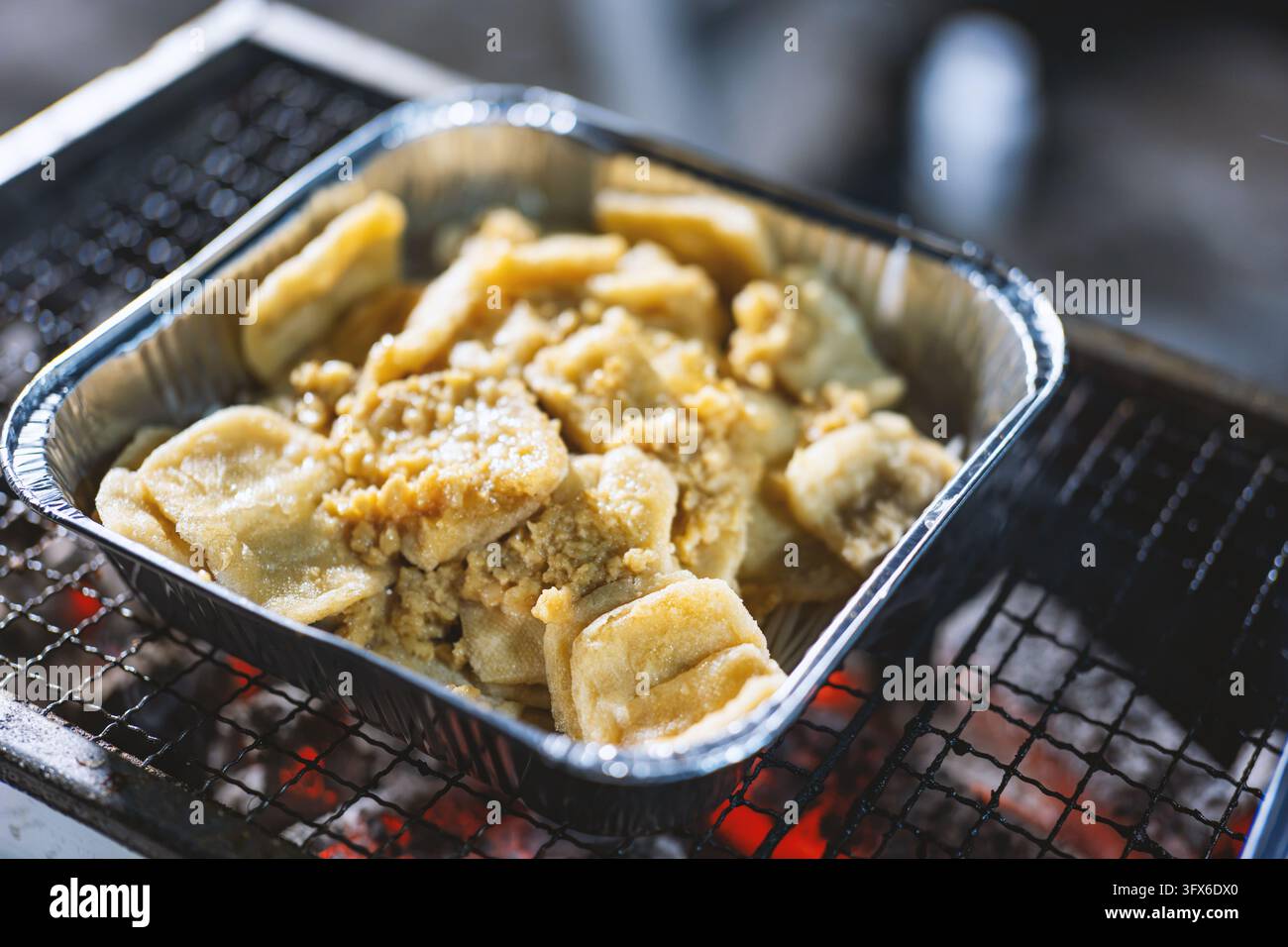 Fishcakes giapponesi Odeng grigliati serviti in un vassoio di alluminio monouso su un barbecue a carboni ardenti, cibo da strada tradizionale con condimento di pasta di pesce sminuzzato saporito e texture dorata, ambientazione di un mercato di strada a Tokyo o Osaka Foto Stock