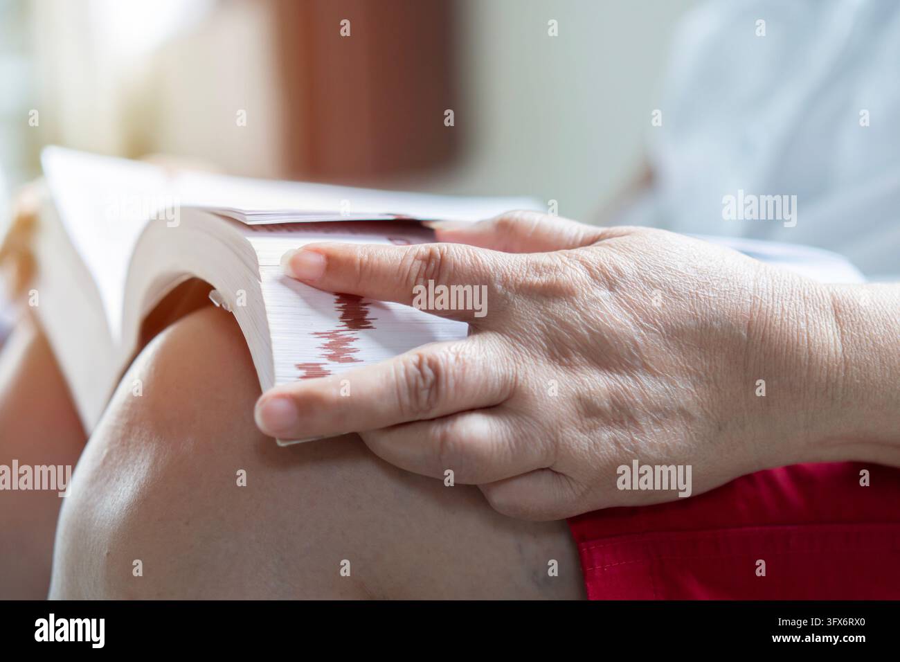 Primo piano di una donna anziana asiatica seduta e che apre un grande libro per leggere a casa. Nonna pensionata che si gode il tempo libero del fine settimana con il suo romanzo preferito da sola Foto Stock