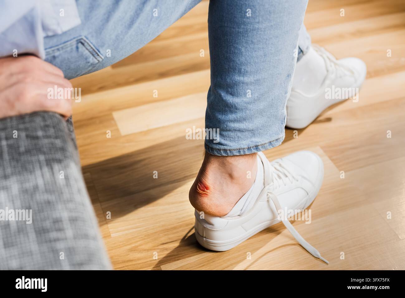 Uomo con una dolorosa vescica al tallone causata da scarpe strette, controlla il piede dolorante, dolore alla camminata e disagio delle scarpe, problema di calzature scomode che richiede b Foto Stock