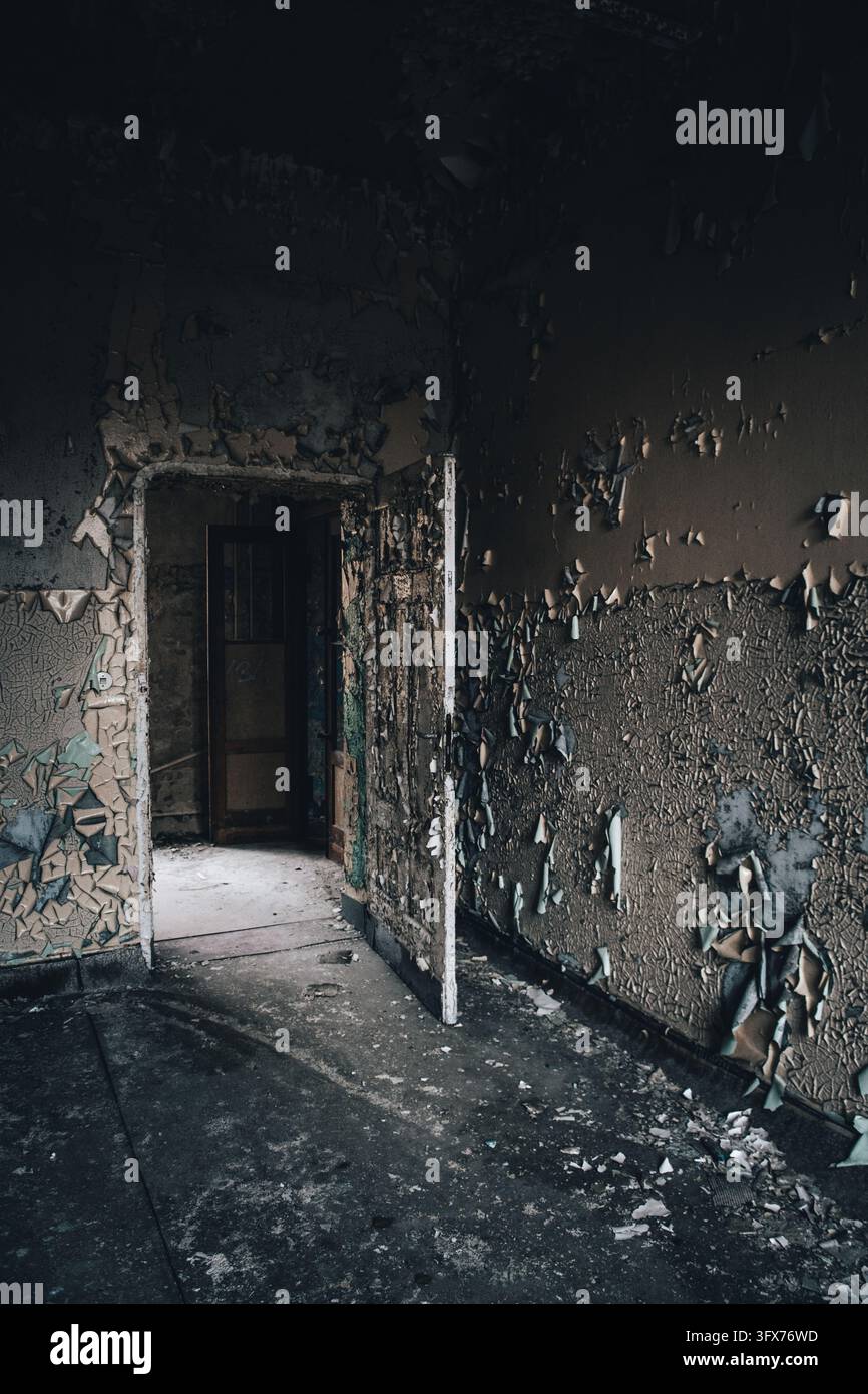 Un corridoio in decadenza in un edificio abbandonato a Berlino, Germania, ha una porta aperta, muri scrostati e detriti sparsi sul pavimento buio. Foto Stock