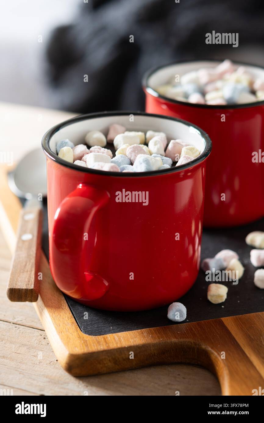 Prima piano di due tazze di ceramica rosse piene di cioccolata calda e mini marshmallow colorati su un tavolo di legno. Foto Stock