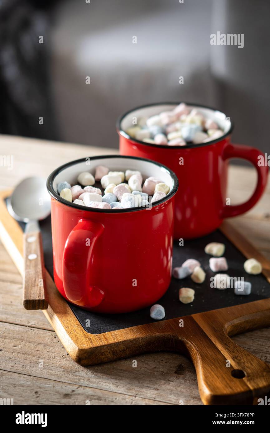 Prima piano di due tazze di ceramica rosse piene di cioccolata calda e mini marshmallow colorati su un tavolo di legno. Foto Stock