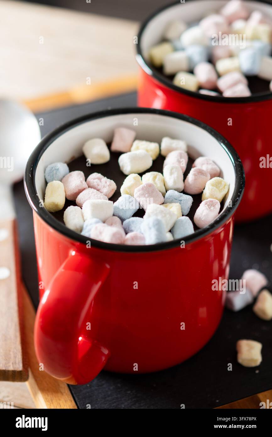 Prima piano di due tazze di ceramica rosse piene di cioccolata calda e mini marshmallow colorati su un tavolo di legno. Foto Stock