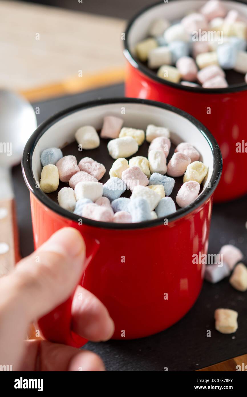 Prima piano di due tazze di ceramica rosse piene di cioccolata calda e mini marshmallow colorati su un tavolo di legno. Foto Stock