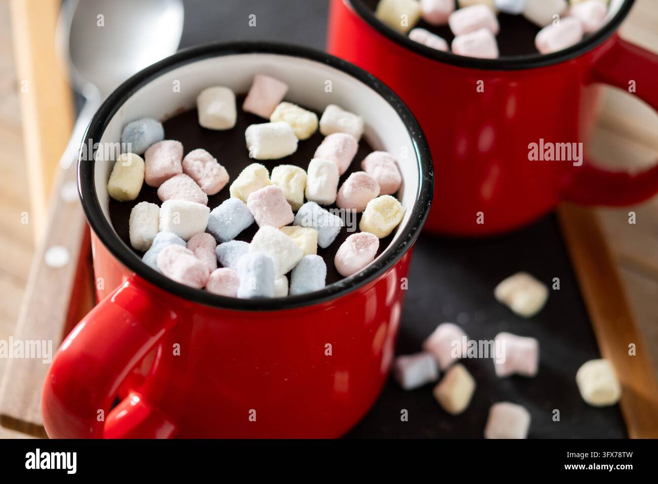 Prima piano di due tazze di ceramica rosse piene di cioccolata calda e mini marshmallow colorati su un tavolo di legno. Foto Stock