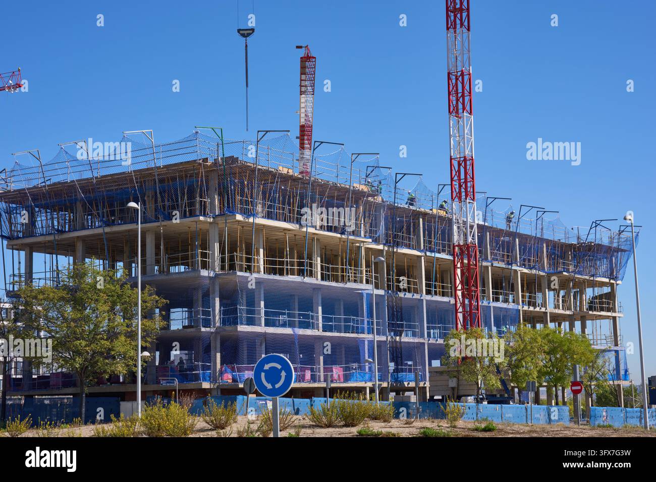 Un edificio a più piani in costruzione con gru, impalcature e reti di sicurezza in una zona urbana soleggiata di Madrid, Spagna, che mostra lo sviluppo urbano Foto Stock