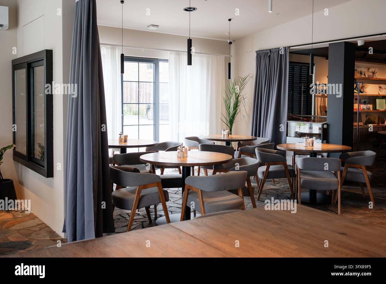 Elegante area da pranzo del caffè vuota con arredamento sofisticato, mobili contemporanei e grandi finestre, perfetta per l'ospitalità e il design d'interni Foto Stock