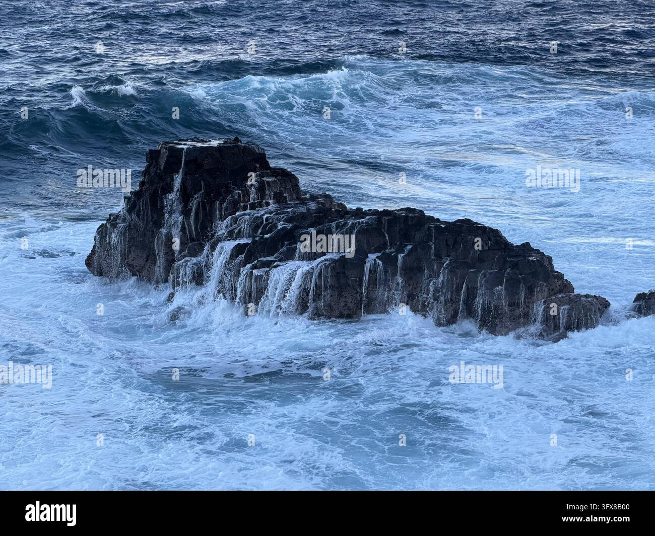 L'acqua schiumosa fuoriesce da una roccia vulcanica scura dopo che un'onda si è infranta lungo la costa frastagliata del sud di Mauritius. - Immagine stock catturata con smartphone