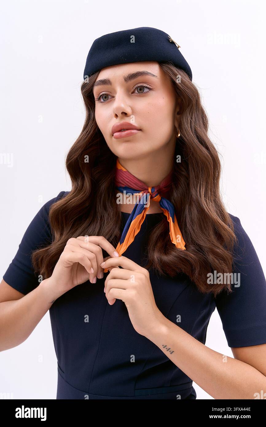 Giovane assistente di volo in un elegante uniforme blu navy si prepara per il viaggio aereo in un ambiente studio luminoso Foto Stock