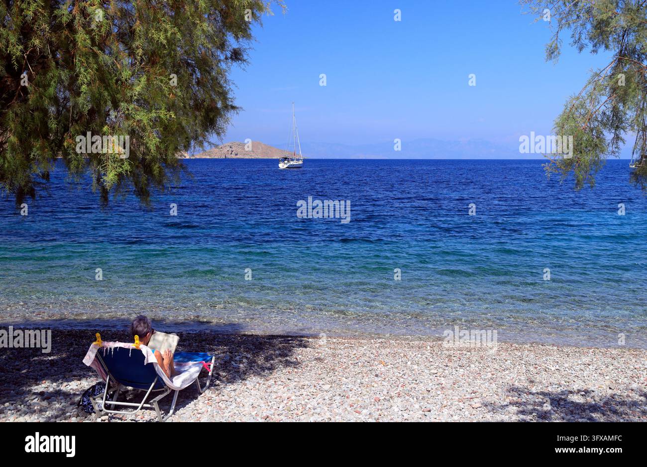 Donna su una sedia da letto che legge libri, Livadia Beach, Tilos, Isole Dodecaneso, Egeo Meridionale, Grecia. Foto Stock