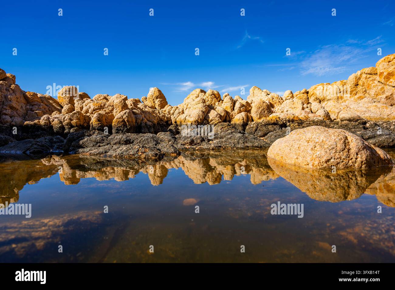 Riflesso di pietre in una pozza d'acqua dai roccioli sulla costa di Marinedda in una giornata di sole, Sardegna, Italia, Europa Foto Stock