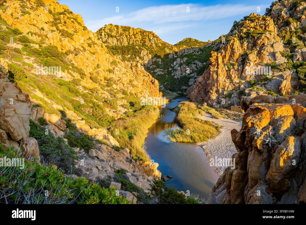 Un piccolo fiume che scorre attraverso le montagne fino al mare, passando davanti a una spiaggia sabbiosa a Costa Paradiso in una serata soleggiata, Sardegna, Italia, Europa Foto Stock