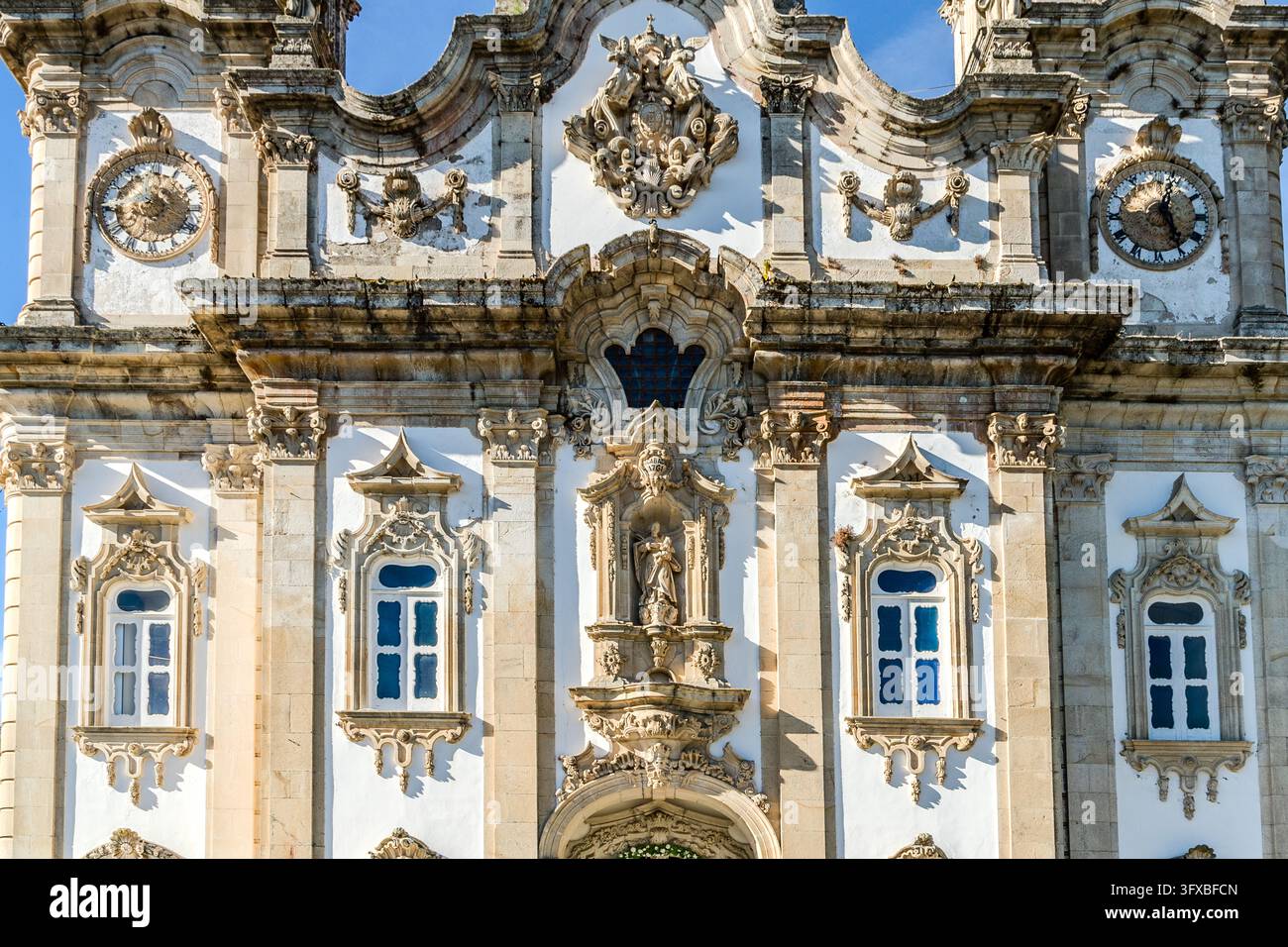 La facciata barocca del Santuário de Nossa Senhora dos Remédios (Santuario di Nostra Signora dei Rimedi) a Lamego, Distretto di Viseu, Portogallo, ha due orologi. Un ornamento e una nicchia con una statua di un santo decorano la facciata. Le finestre hanno vetro blu. Foto Stock
