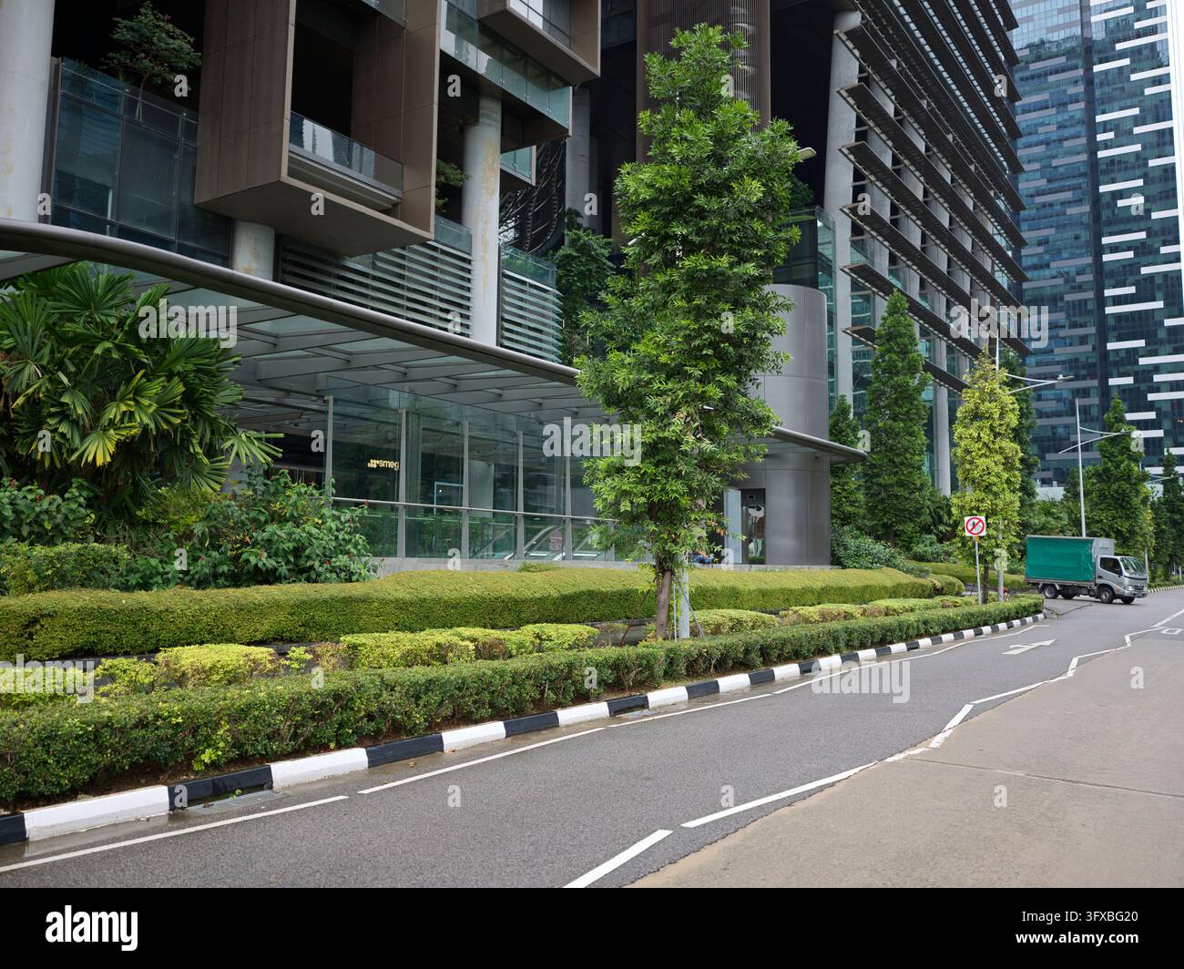 Strada paesaggistica con siepi e alberi accanto a un grattacielo moderno a Singapore. Foto Stock