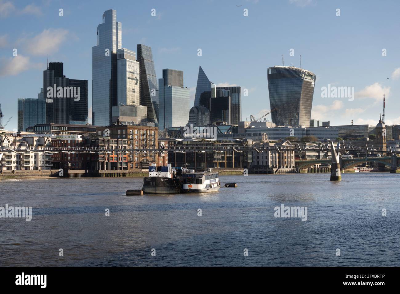 Le barche navigano il Tamigi oltre il Millennium Bridge, mostrando lo skyline. Questo è stato scattato a Bankside, Londra. Foto Stock