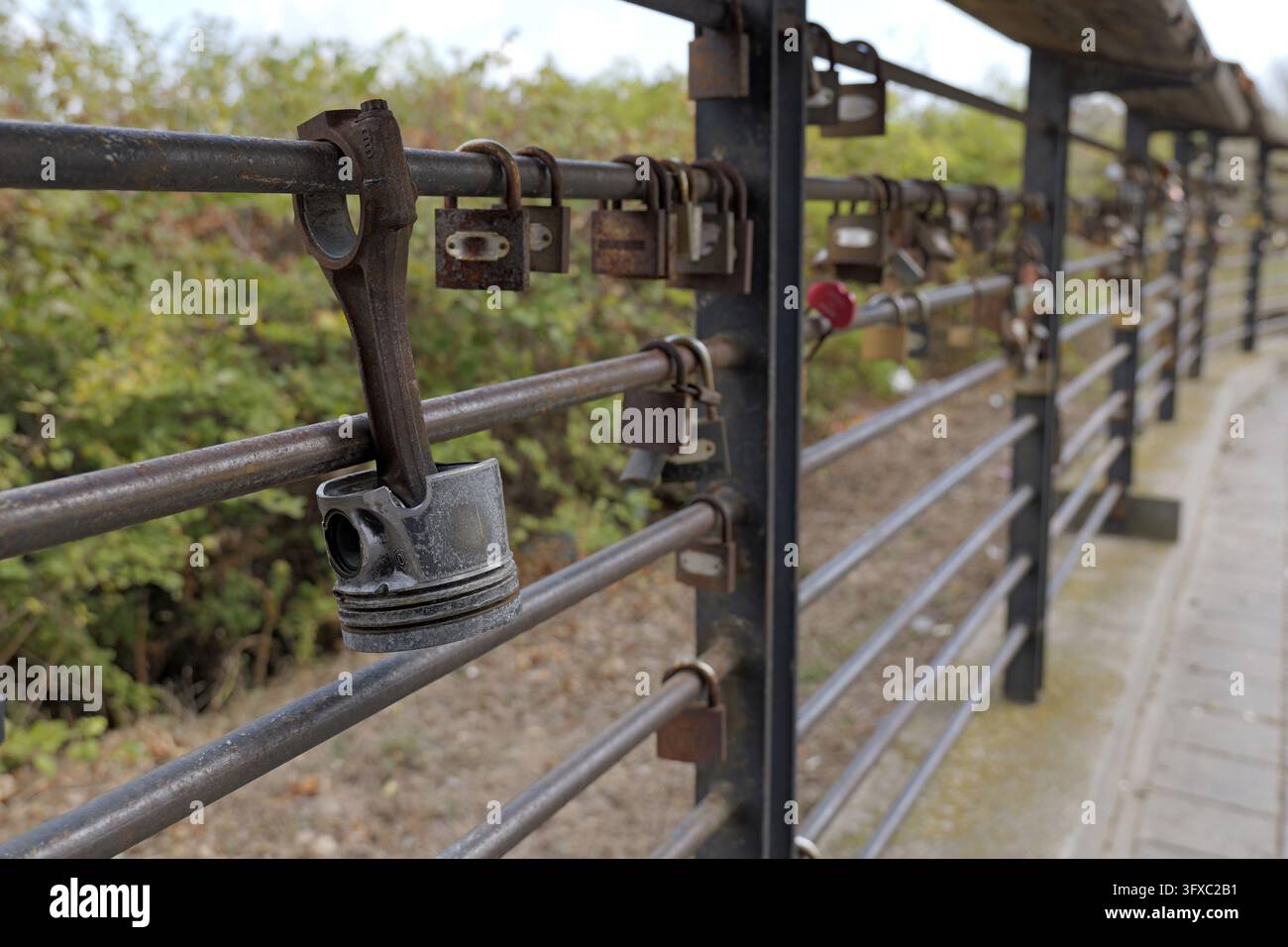Pistone e numerosi lucchetti arrugginiti che simboleggiano l'amore e l'impegno appesi a una recinzione di un ponte metallico, rappresentando relazioni durature e ricordi condivisi Foto Stock
