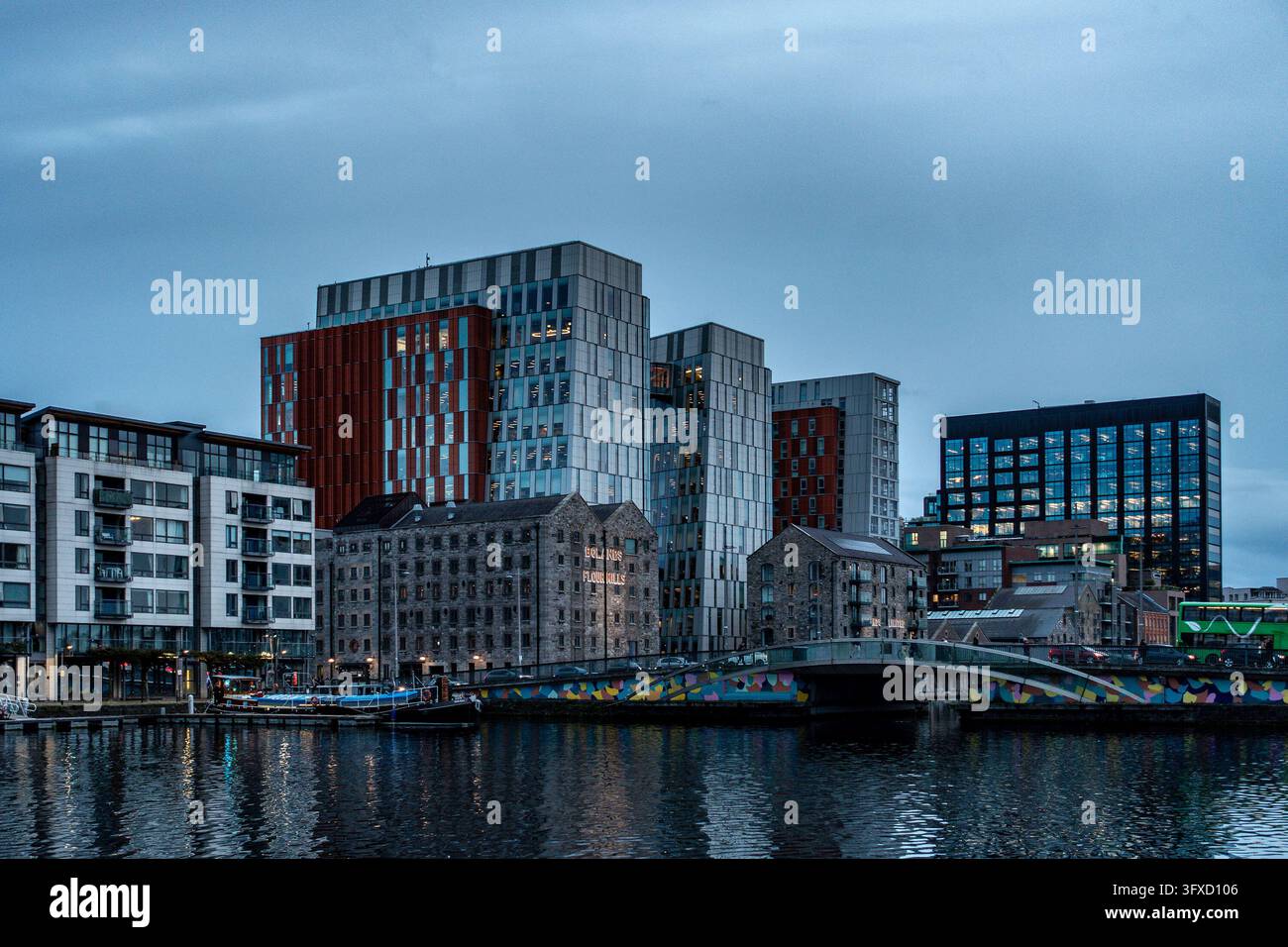 Complesso di uffici Google al restaurato Bolands Mills, Grand Canal Dock a Dublino, riflesso nell'acqua al crepuscolo oltre un ponte colorato. Foto Stock
