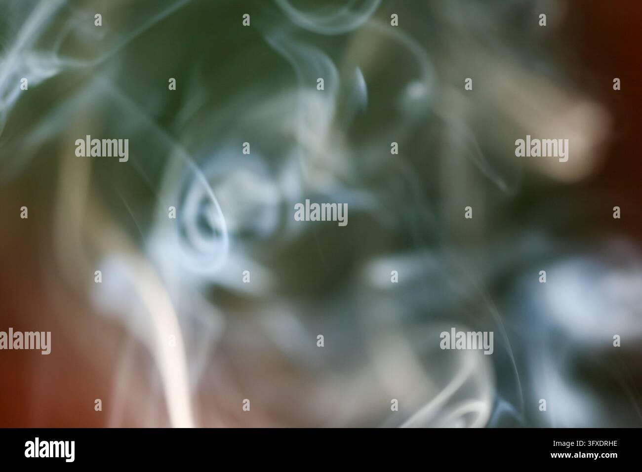 Fumo bianco e vaporeoso che si snoda attraverso un campo morbido e sfocato di toni verdi, ruggine e carbone, creando uno sfondo astratto etereo con vapore fluido Foto Stock