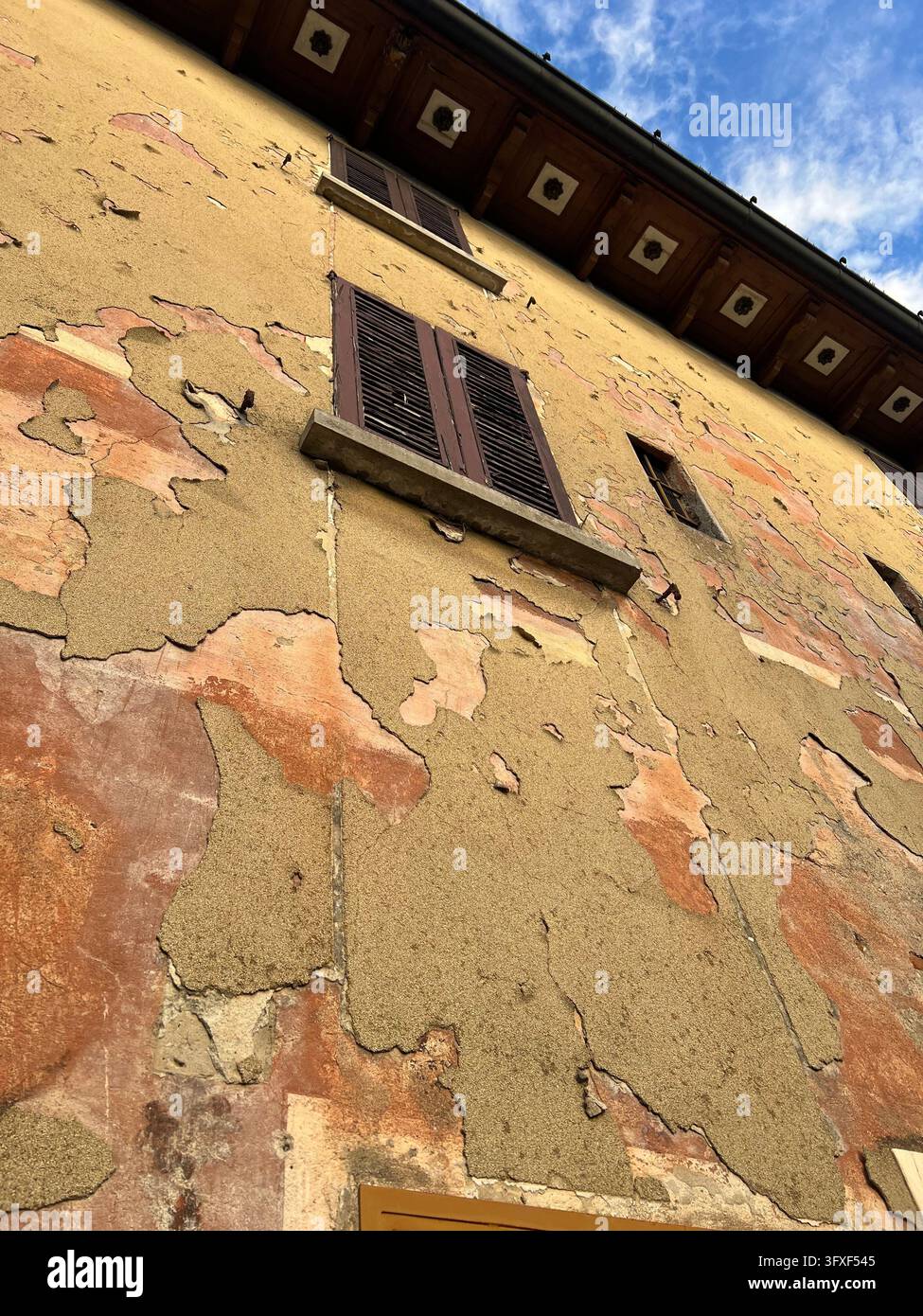 Facciata consumata di un antico edificio italiano con intonaco scolorito e persiane di legno Foto Stock