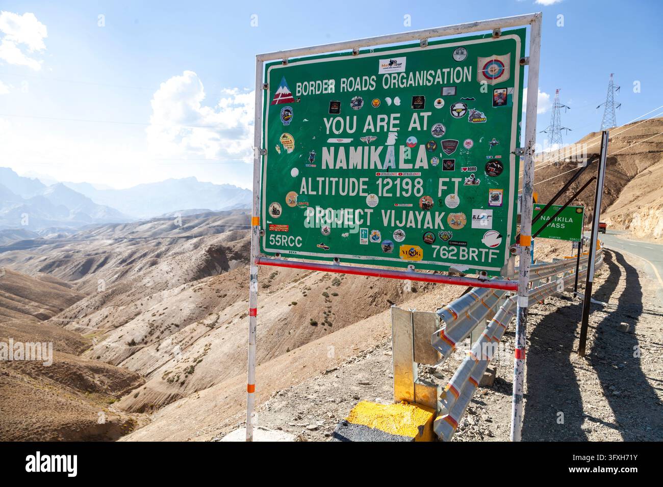 Segnale stradale verde coperto di adesivi di viaggio a un alto passo di montagna, Ladakh, Nimikala, India Foto Stock