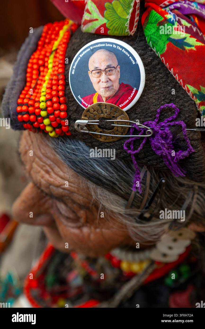 Profilo di una donna anziana della tribù Brokpa che indossa un berretto con perline e un badge con il ritratto del Dalai Lama e una spilla di sicurezza, Ladakh, Dha, India Foto Stock