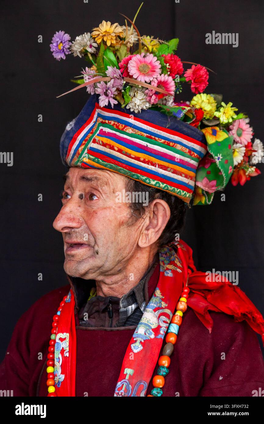 Profilo di un uomo anziano della tribù Brokpa con un berretto a righe sormontato da fiori colorati, Ladakh, Dha, India Foto Stock
