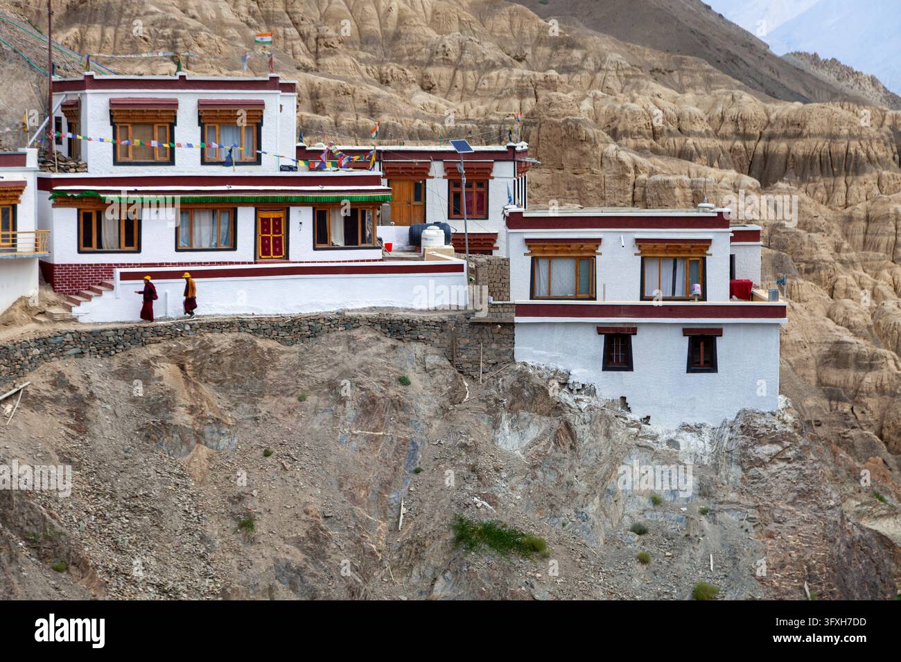 Due monaci che passano davanti ad edifici monastici bianchi su una scogliera erosa al Monastero Yuru, Ladakh, Lamayuru, India Foto Stock