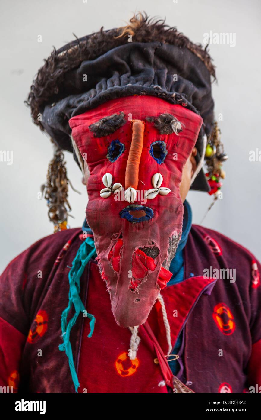 Figura mascherata che indossa una maschera di stoffa rossa decorata con conchiglie di cauri e un cappello di pelliccia durante il festival di Ladakh, Ladakh, Leh, India Foto Stock
