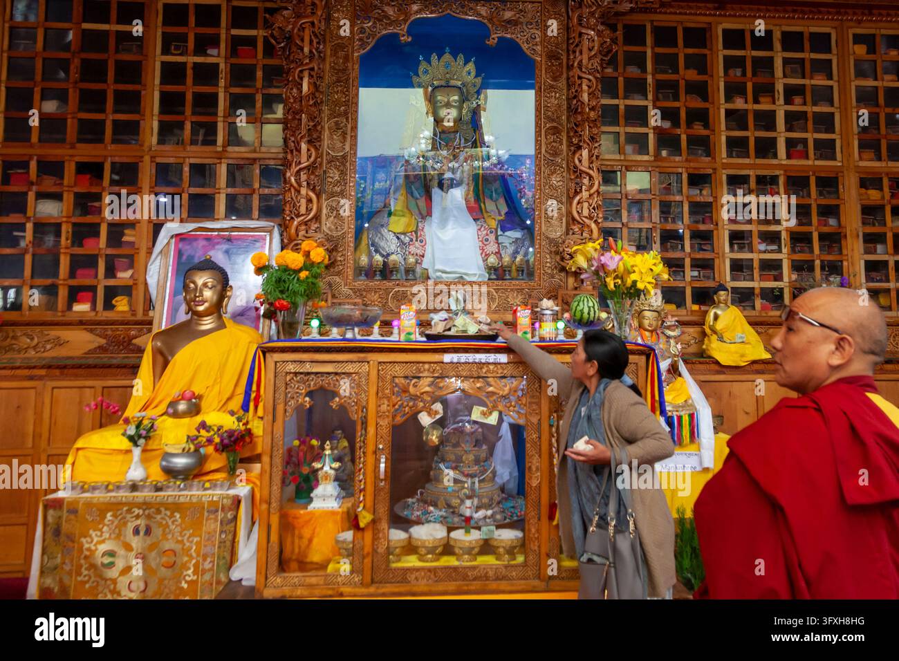 Donna che posa un'offerta su un altare del tempio con statue di Buddha accanto a un monaco, Ladakh, Leh, India Foto Stock