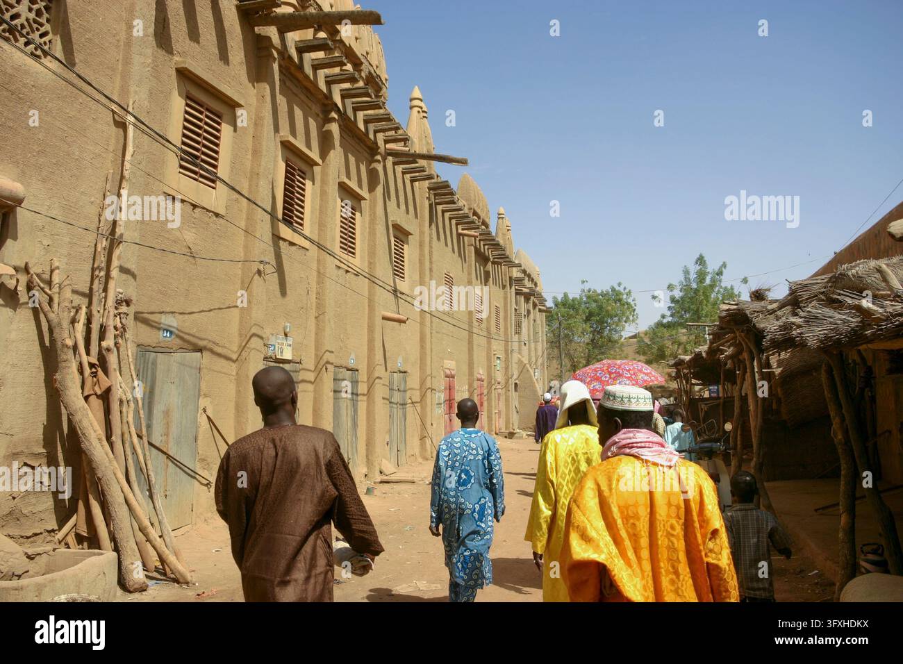 Uomini in abiti colorati che camminano lungo una strada fiancheggiata da edifici tradizionali in fango, regione di Mopti, Djenne, Mali Foto Stock