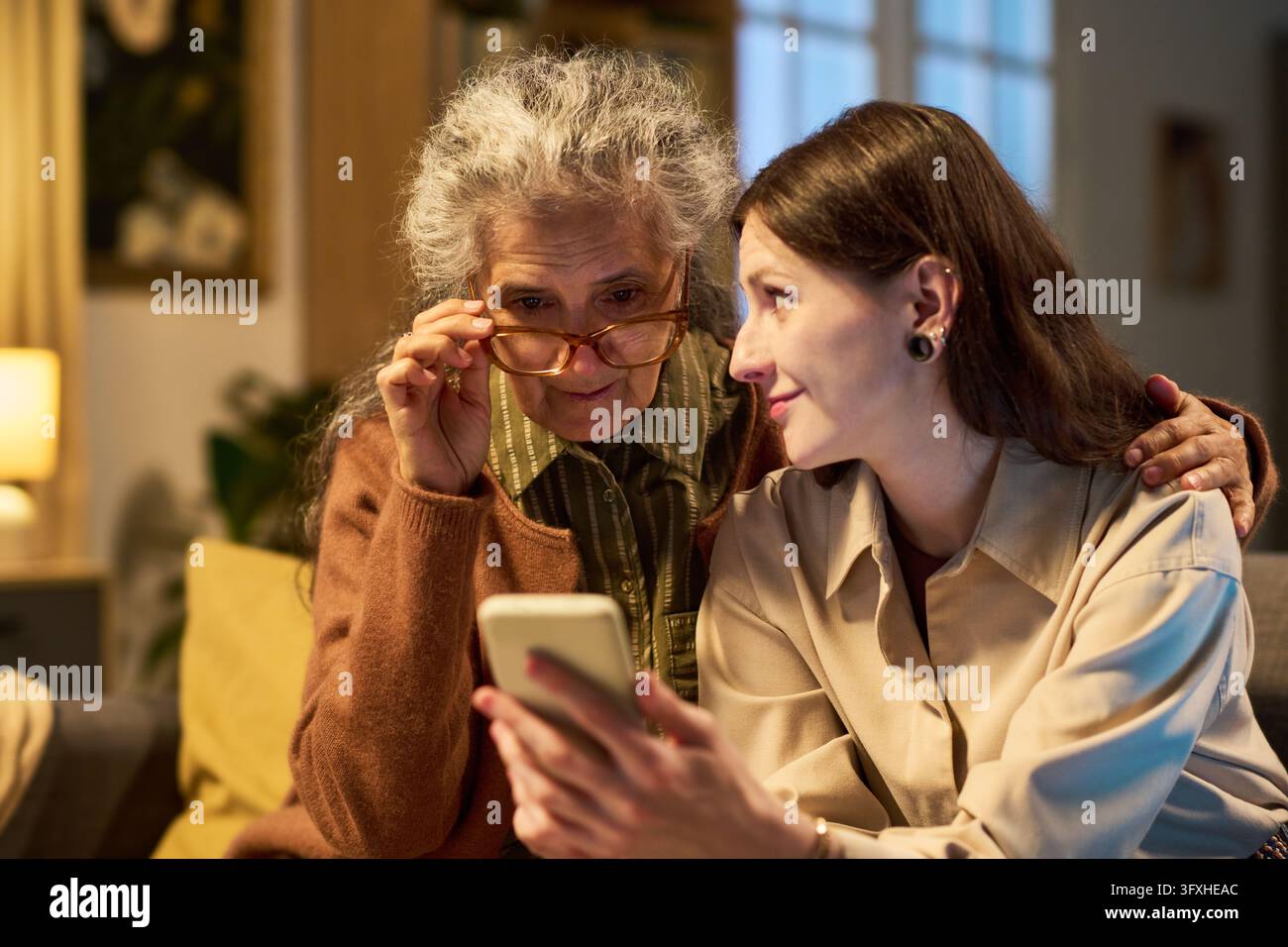 Donna anziana e figlia adulta che utilizzano lo smartphone a casa Foto Stock
