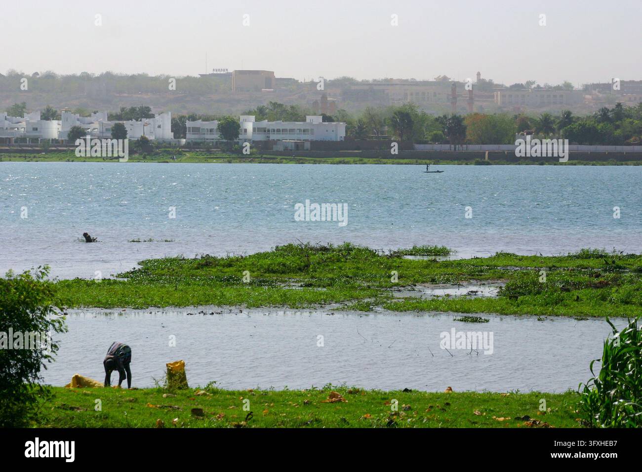 Persone che si lavano sulla riva erbosa del fiume Niger di fronte agli edifici bianchi sull'altra riva, distretto di Bamako, Bamako, Mali Foto Stock